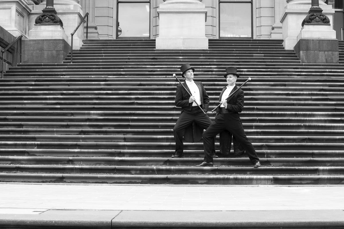 Two men in top hats and tuxedos stand on Parliament steps. They are pulling funny faces.