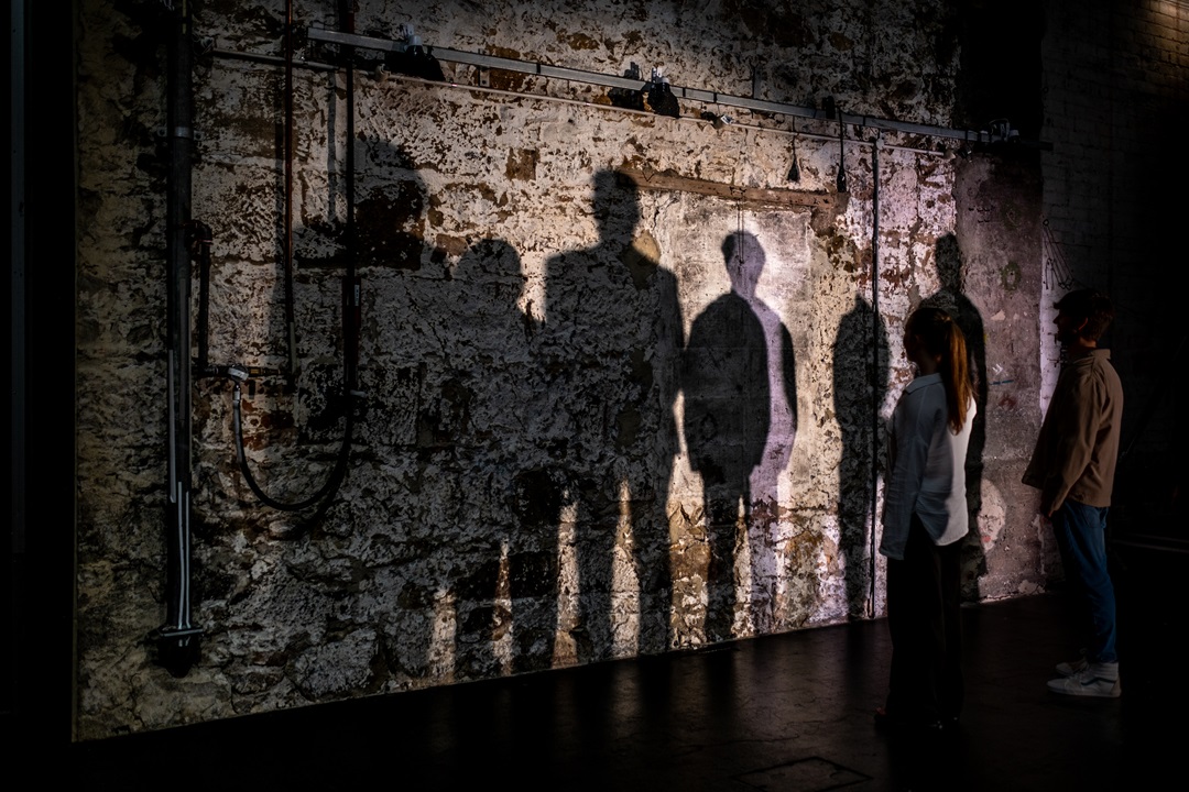 Shadowy silhouettes are seen against a rustic sandstone wall.