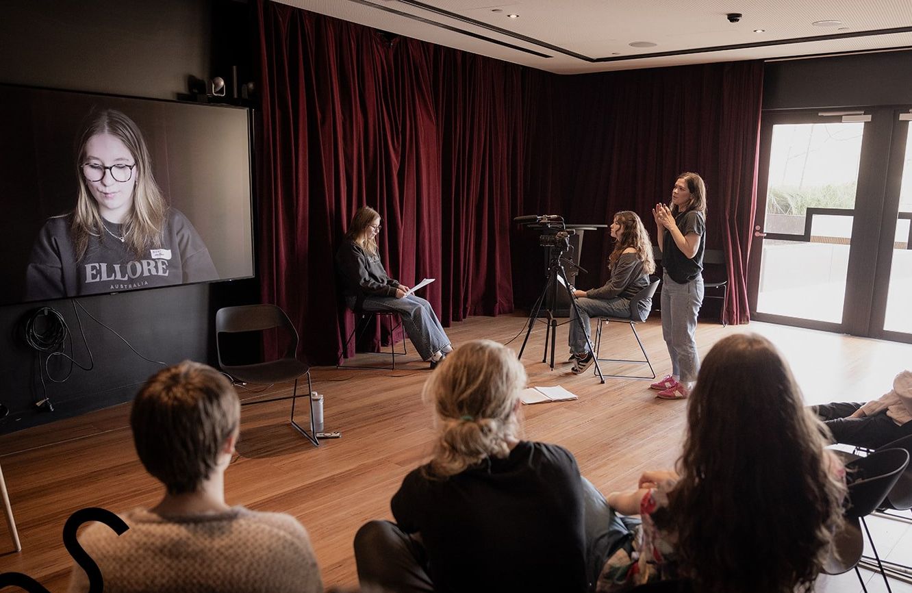 A teenage student presents a work on a large screen to other students and mentors