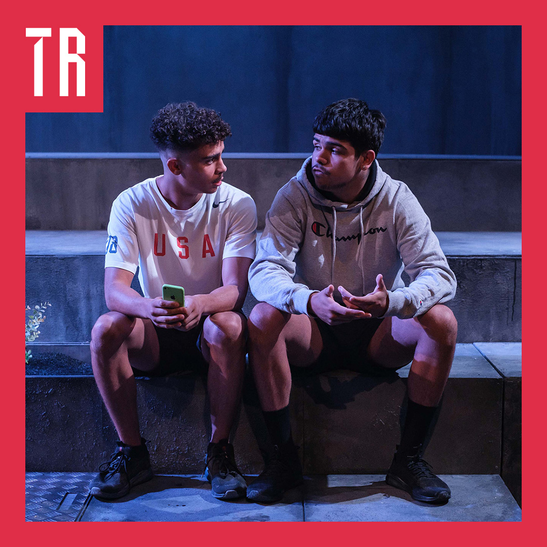Two teenage First Nations boys sit on a step, they are deep in conversation