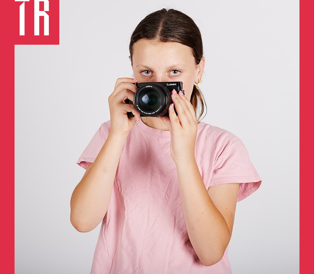 Photo: Lucy Parakhina A teenage girl holds a camera in front of her face, her eyes can been seen over the top of the camera looking directly at us