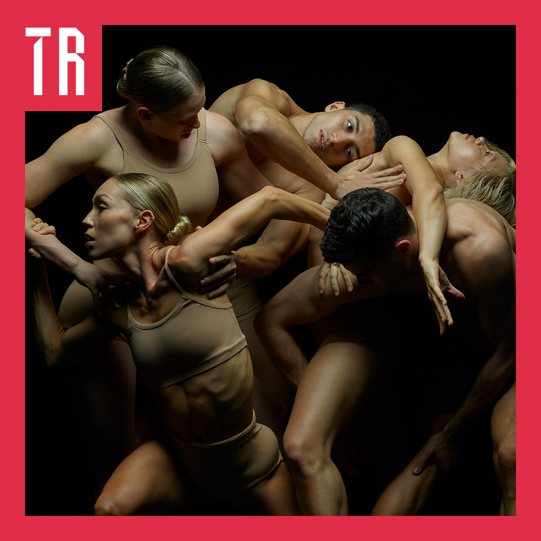Image: Jez Smith A dramatic, high-contrast studio photograph of five contemporary dancers wearing beige, skin-toned athletic crop tops and briefs against a stark black background. The dancers are closely intertwined in an intricate, dynamic cluster, their bodies, arms, and legs overlapping in fluid, expressive motion. Strong studio lighting accentuates their muscular tone and physical form. The image is framed by a bold, hot-pink border, with a stylized white logo containing the letters "TR" in the upper-left corner.