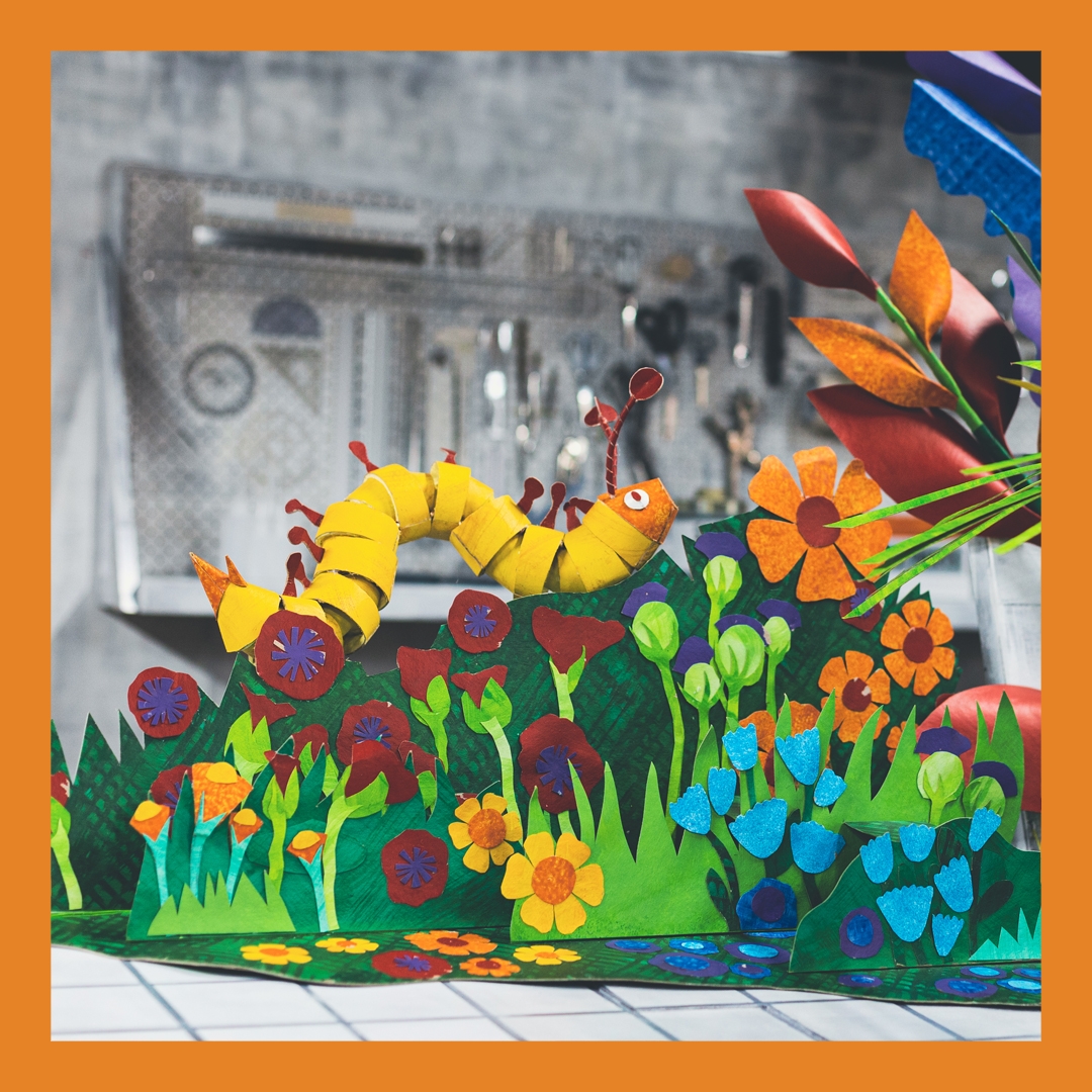 Photo: Darcie Richards A paper caterpiller sits in a brightly coloured paper garden.