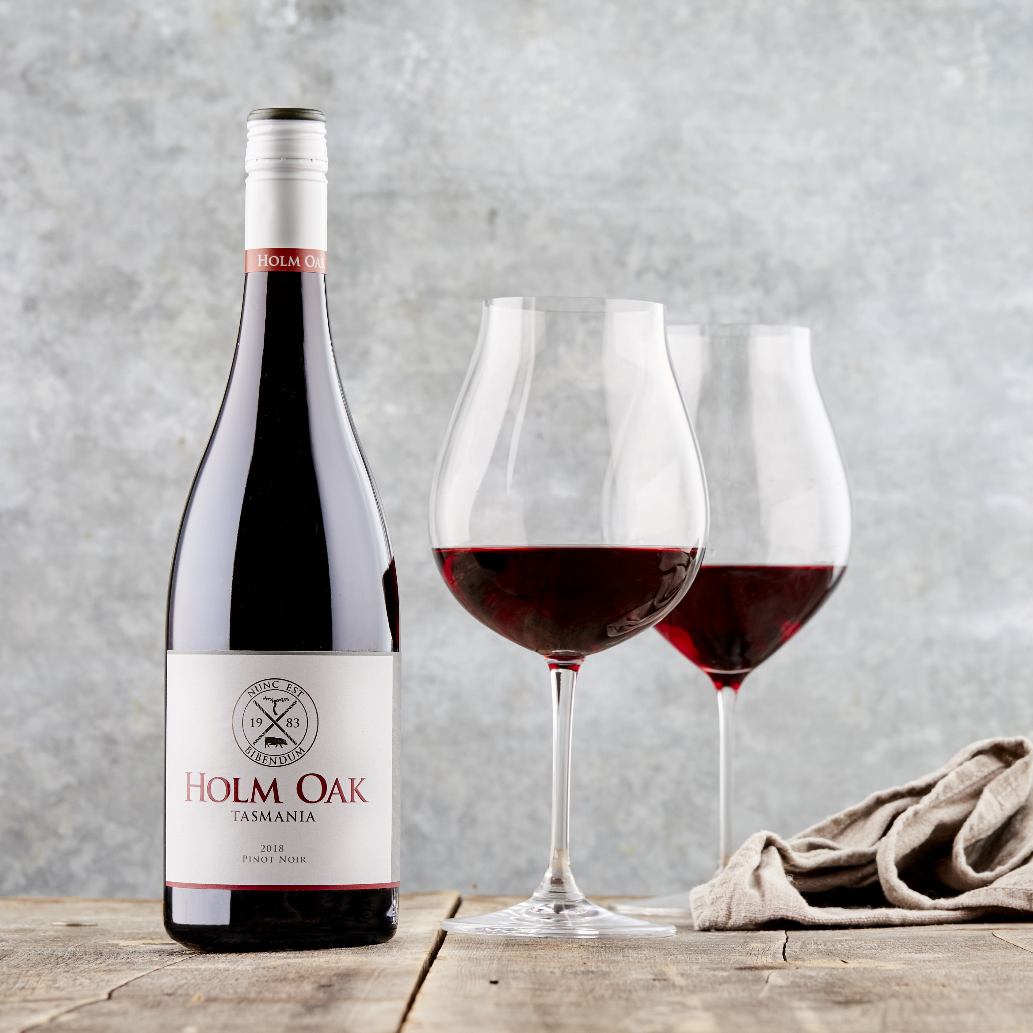 A bottle of red wine and two glasses sit on a table. There is a rumpled napkin next to them, in a beige colour.
