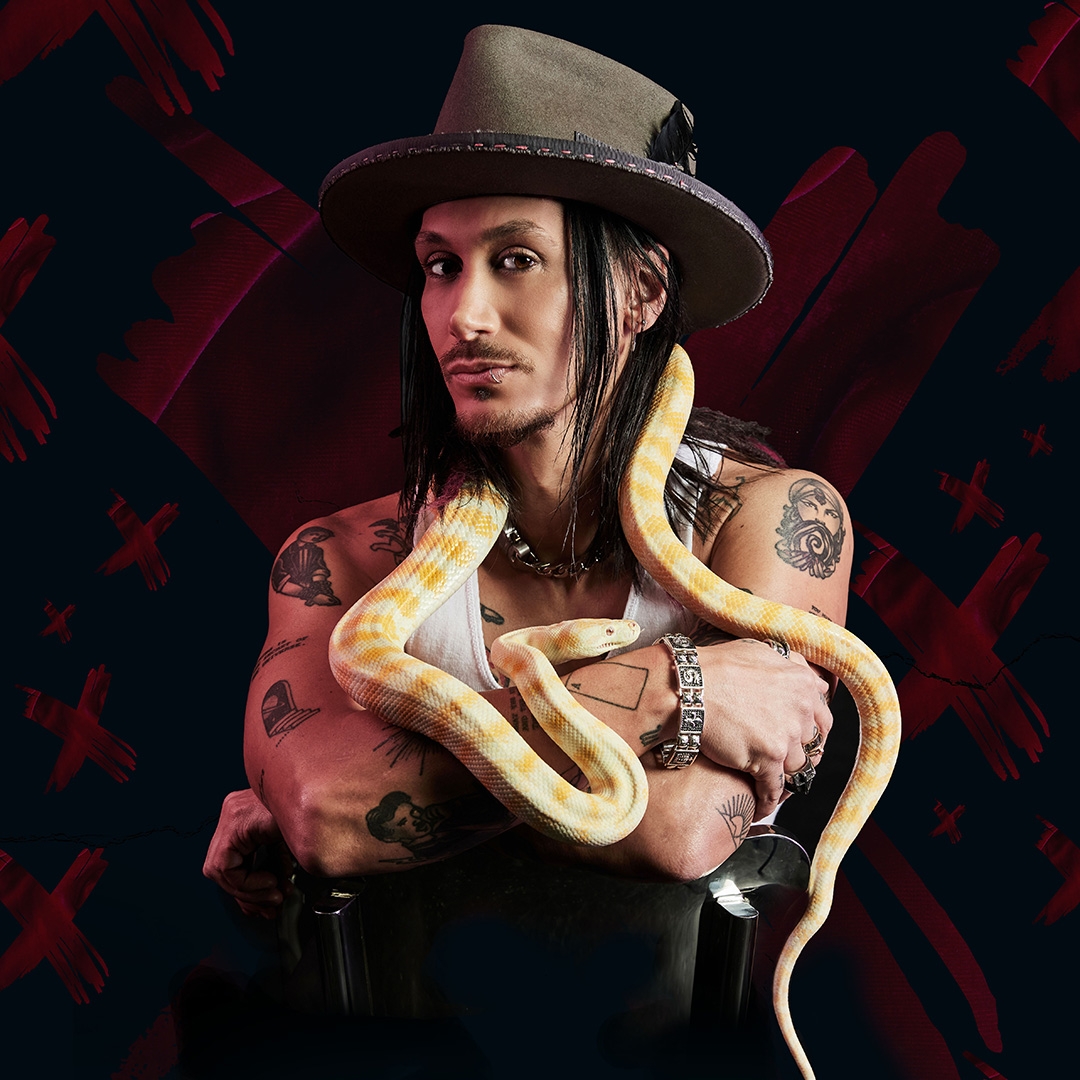 A man wearing a grey slouch hat is adorned by a golden snake