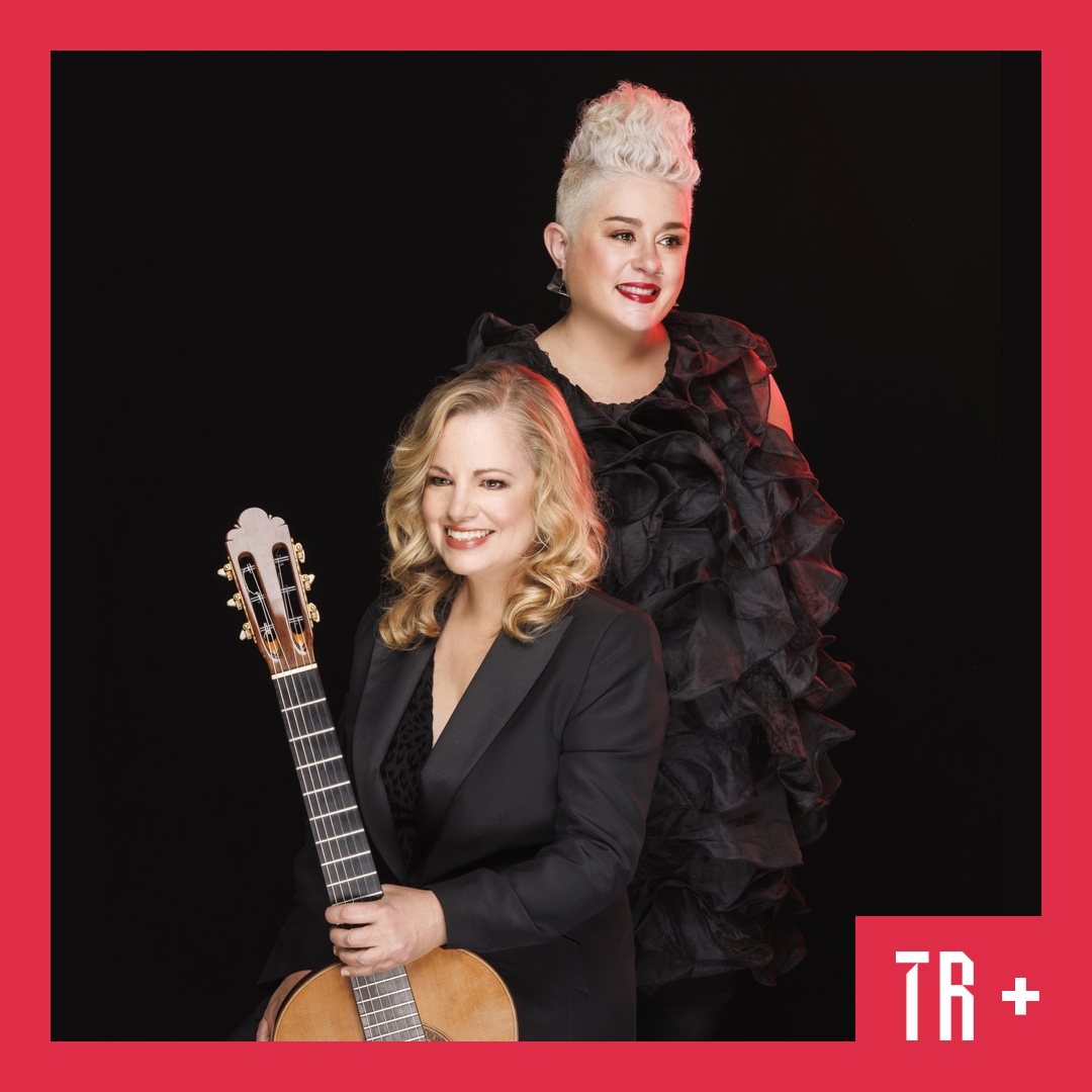 Katie Noonan HERO Two women stand against a black background, one is holding a guitar