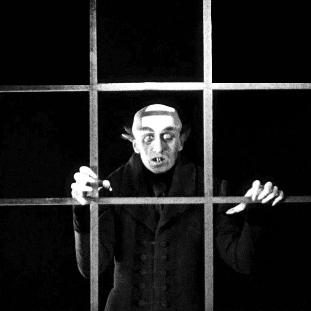 Nosferatu HERO image A black and white image of a monsterous human live creature with a white bald head and long menacing nails stands agains a black background