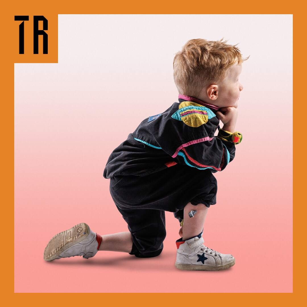 Photo: Darren Gill A boy kneels on one knee. He looks off into the distance. He is wearing active gear and the background is a gradient from peach at the bottom to white at the top. There is an orche coloured border on the image and the Theatre Royal logo is in the top left of the image.