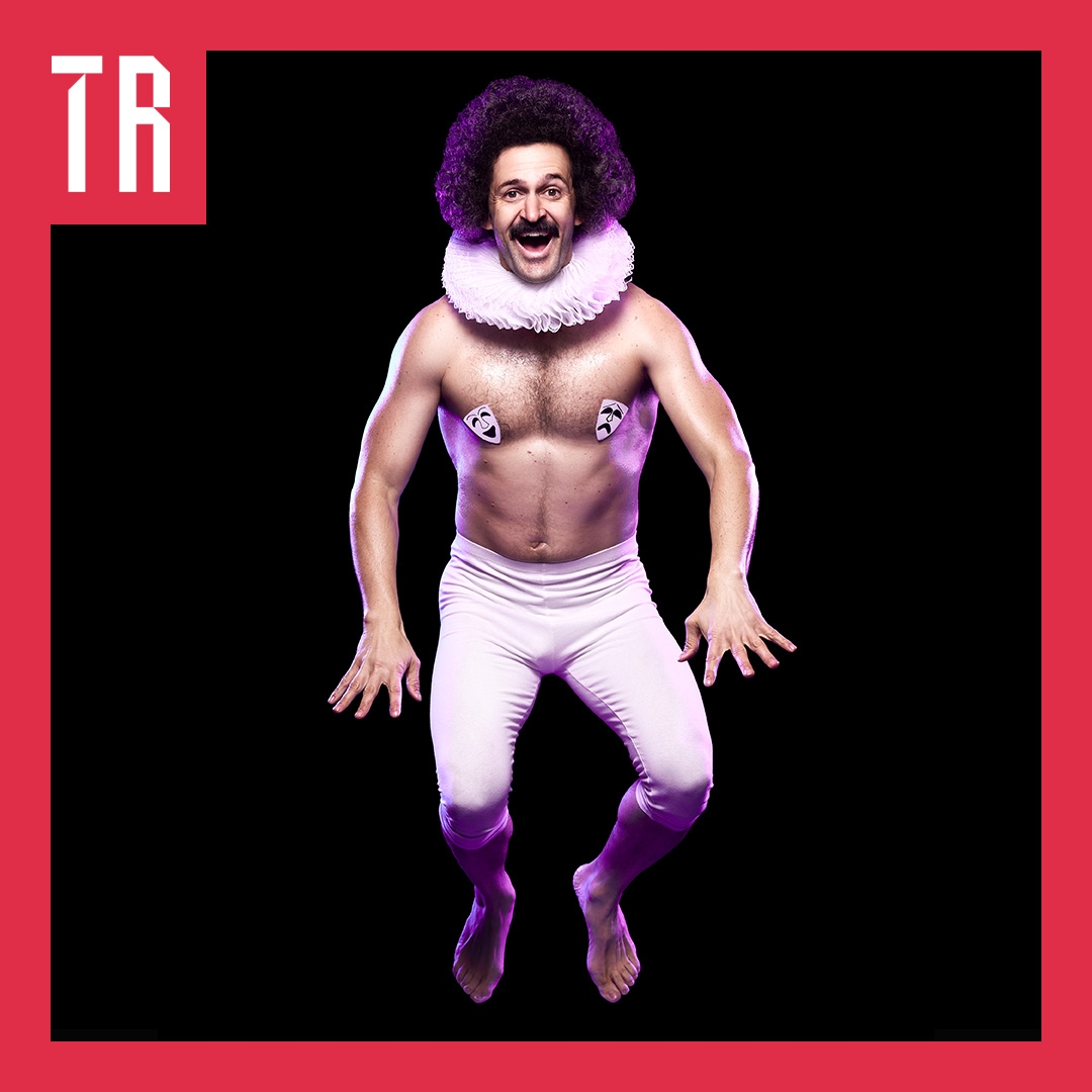 Photo: Aaron Walker A man jumping in baby pink tights with an Elizabethan ruff around his neck. He has a big curly afro and moustach and looks strong