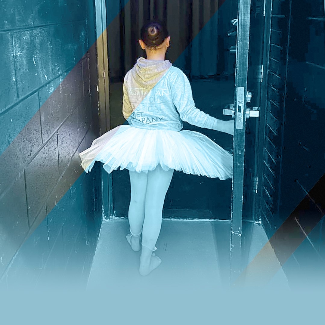 Marketing ballet hero image A young ballerina is walking through a door. She wears a large tutu skirt and a hooded top