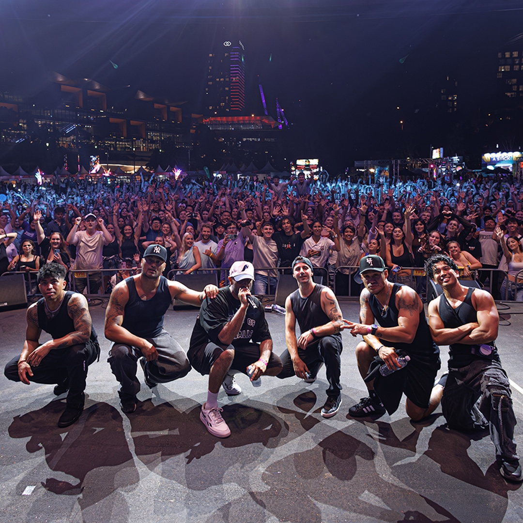 Image: supplied A group of 6 urban music performers crouch on a stage in a semi circle. Behind them a large crowd cheers