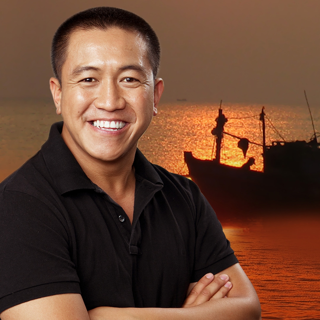 Image: supplied A portrait picture of Anh Do standing in front of a water sunset with and asian fishing boat shilouette