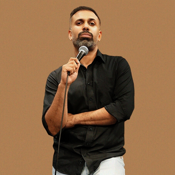 Image: supplied A portrait of comedian Pritish Narula, he is wearing a black shirt ans is holding a microphone