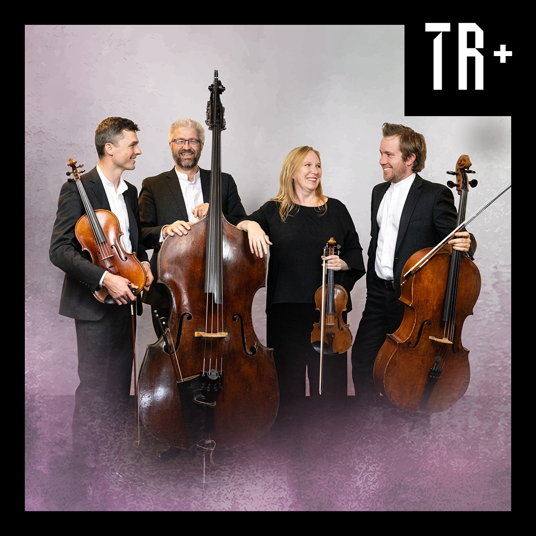 Four musicians stand holding clasical instruments. They are wearing black and white formal wear but have a relaxed and comfortable air about them