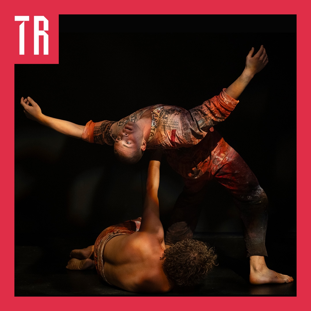 This photo looks like a Carravagio painting, two dancers appear on a black bacground, on is lying on the ground with their back to us, arm raised supporting the second dancer as the bend backwards as if falling