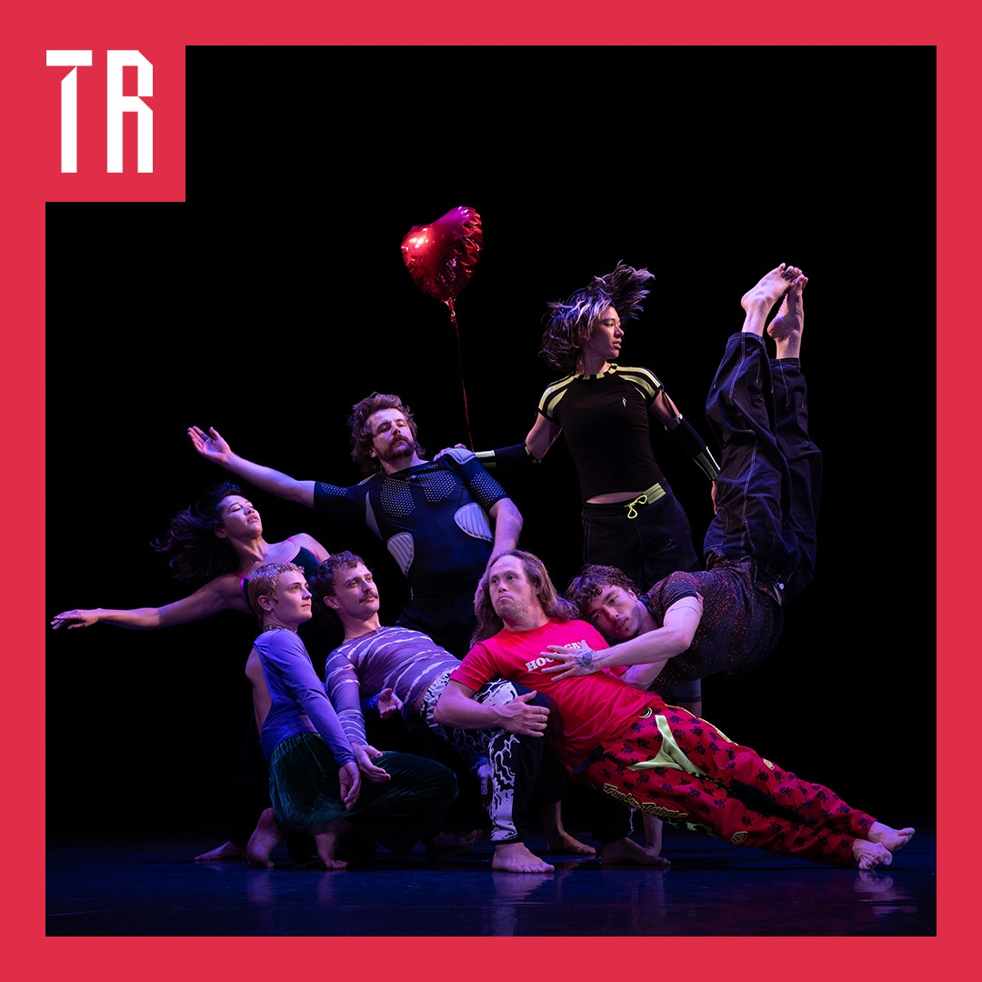 A group of seven dancers emerge from a black backgroun, the huddle and sprawl against each other, the image is dynamic and interesting