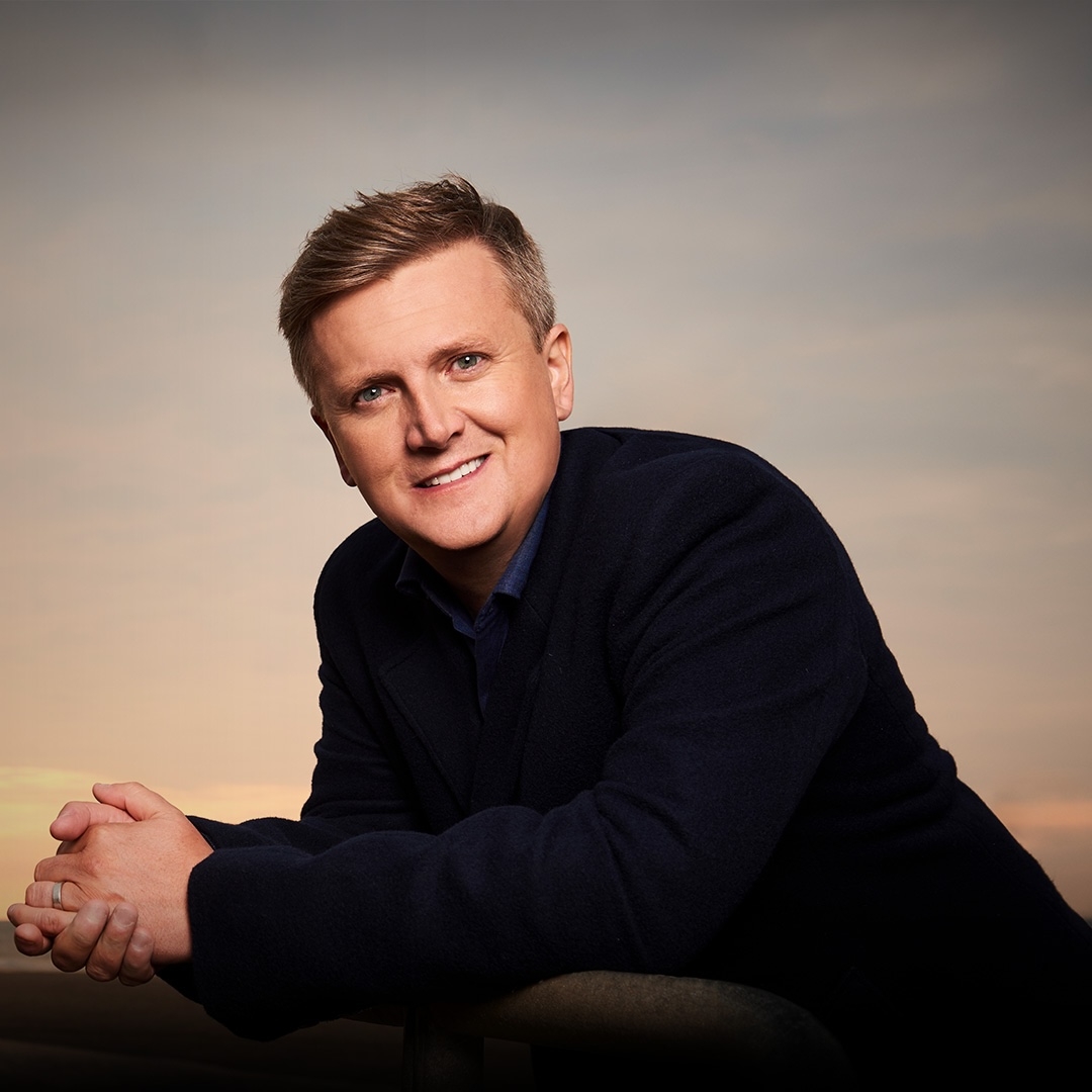 Portrait of singer Aled Jones, wearing a black sweater agains a dusk sky