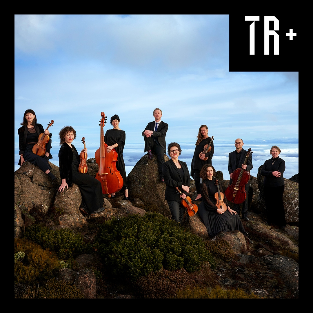 Members of Van Diemen's Band perrch on mountain bounlders on Kunyani, they hold their instruments, behind them the sky stretches into the horizon
