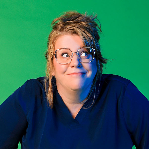 Portrait of comedian Georgie Carroll looking mischievious on a bright green back ground