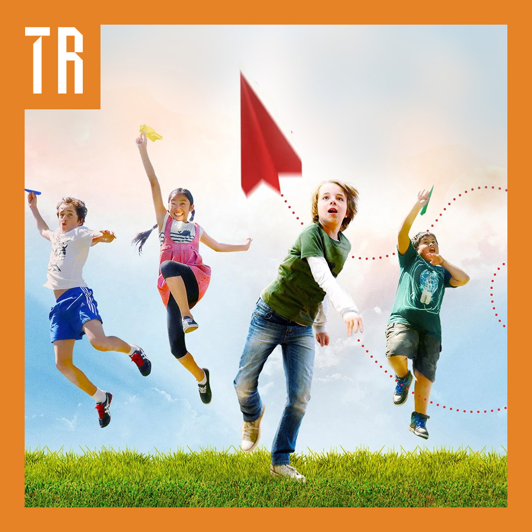 A group of four children a frozen mid jump as they throw paper planes in the air