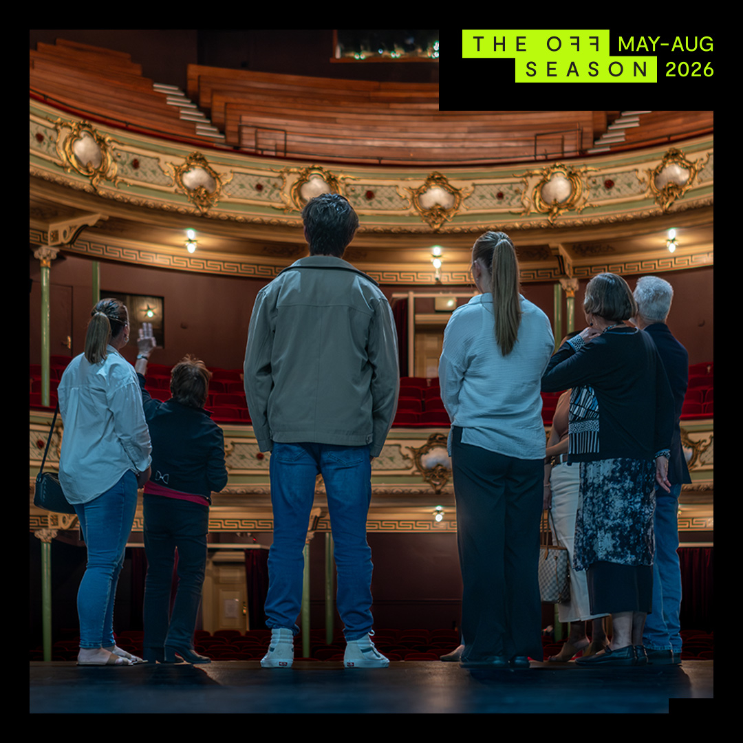 A group of visitors stand on the Theatre Royal stage looking out at the opulant stalls and seating