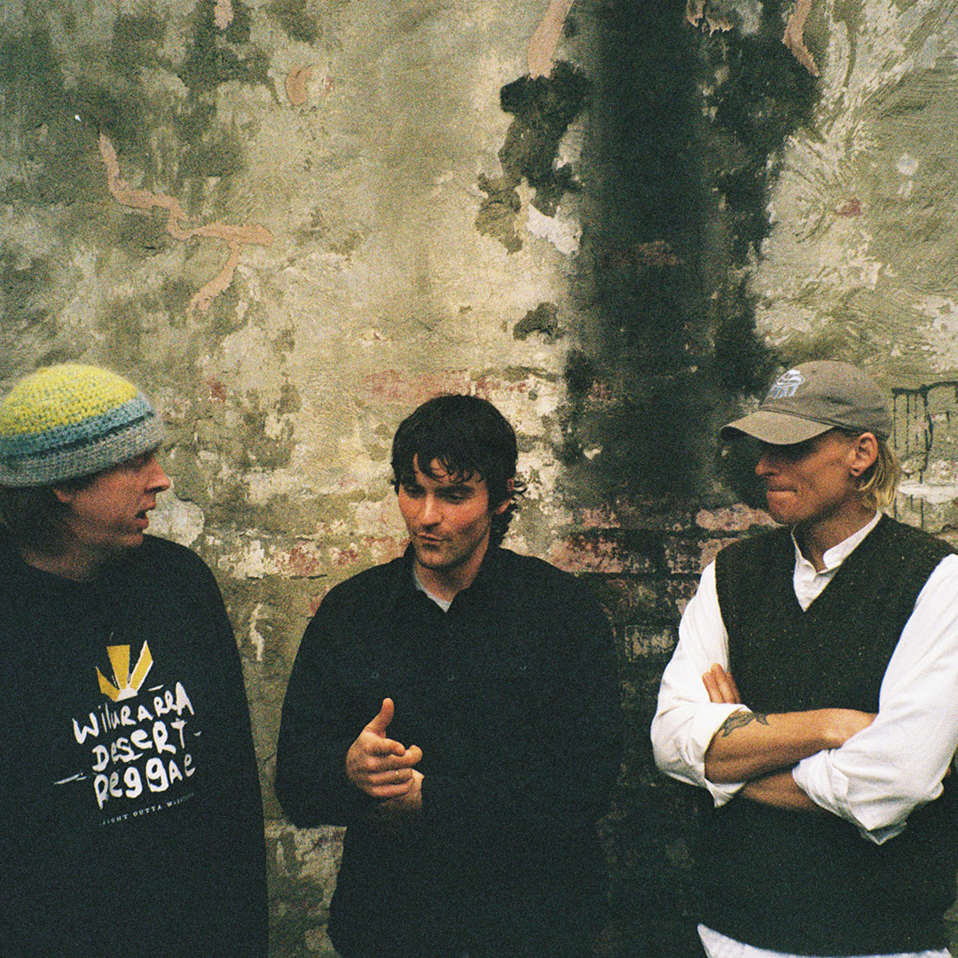 Three young male musicians stand together in an informal but friendly way.