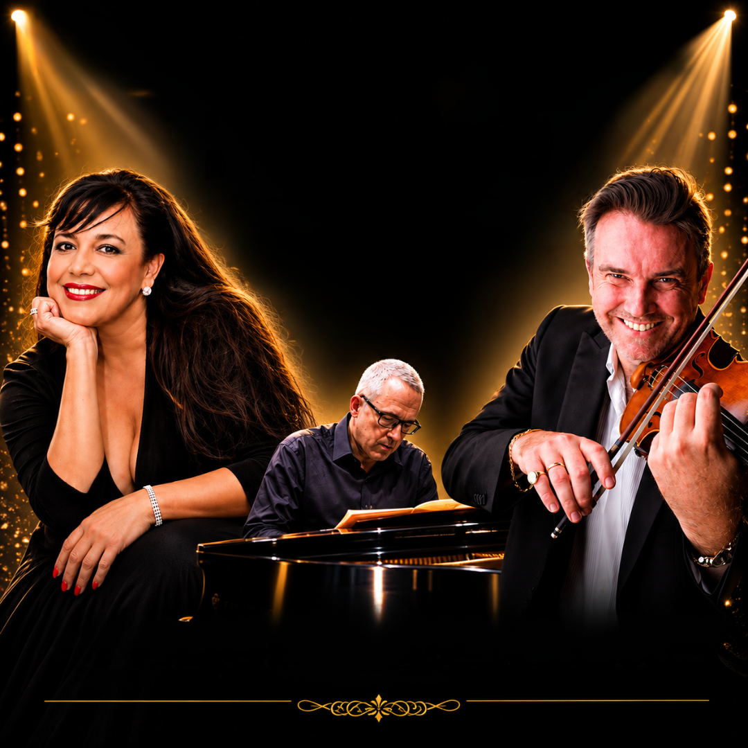 A promotional portrait of three musicians under warm golden stage lights against a black background. On the left, Penny Pavlakis smiles while resting her chin on her hand. In the centre, special guest Clemens Leske sits at a grand piano. On the right, Vov Dylan smiles while playing the violin. Golden spotlights and glowing particles frame the performers.