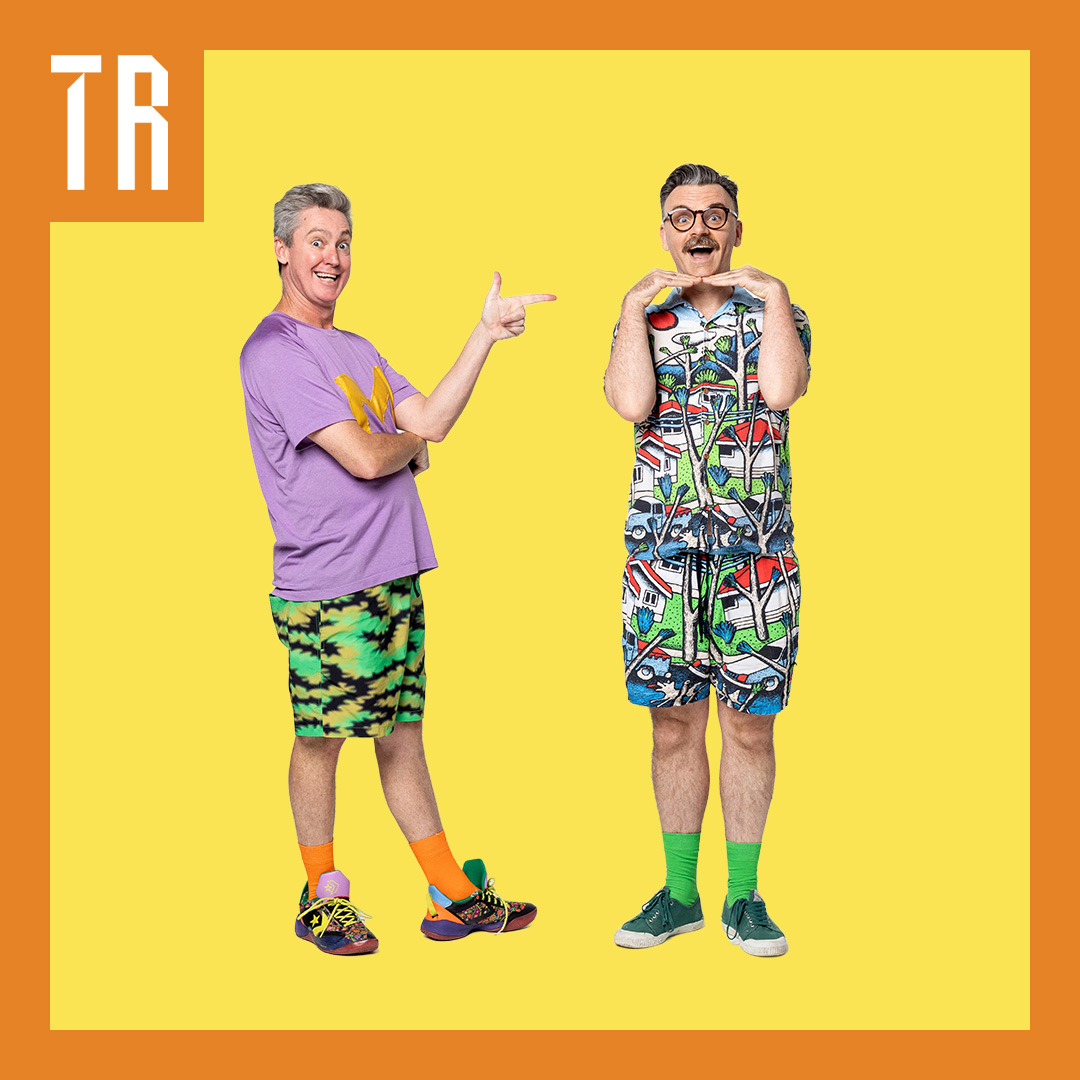 Two men in colorful, playful outfits pose against a yellow background, each tilting their head and framing their face with their hands. A orange border and white “TR” lettering appear along the left side.