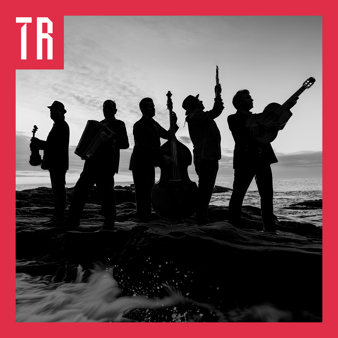 Black-and-white photograph of five silhouetted musicians performing on rocky shore at sunset, playing violin, accordion, double bass, and guitar, with ocean waves behind them. A red border surrounds the image, with a white “TR” logo in the upper-left corner.