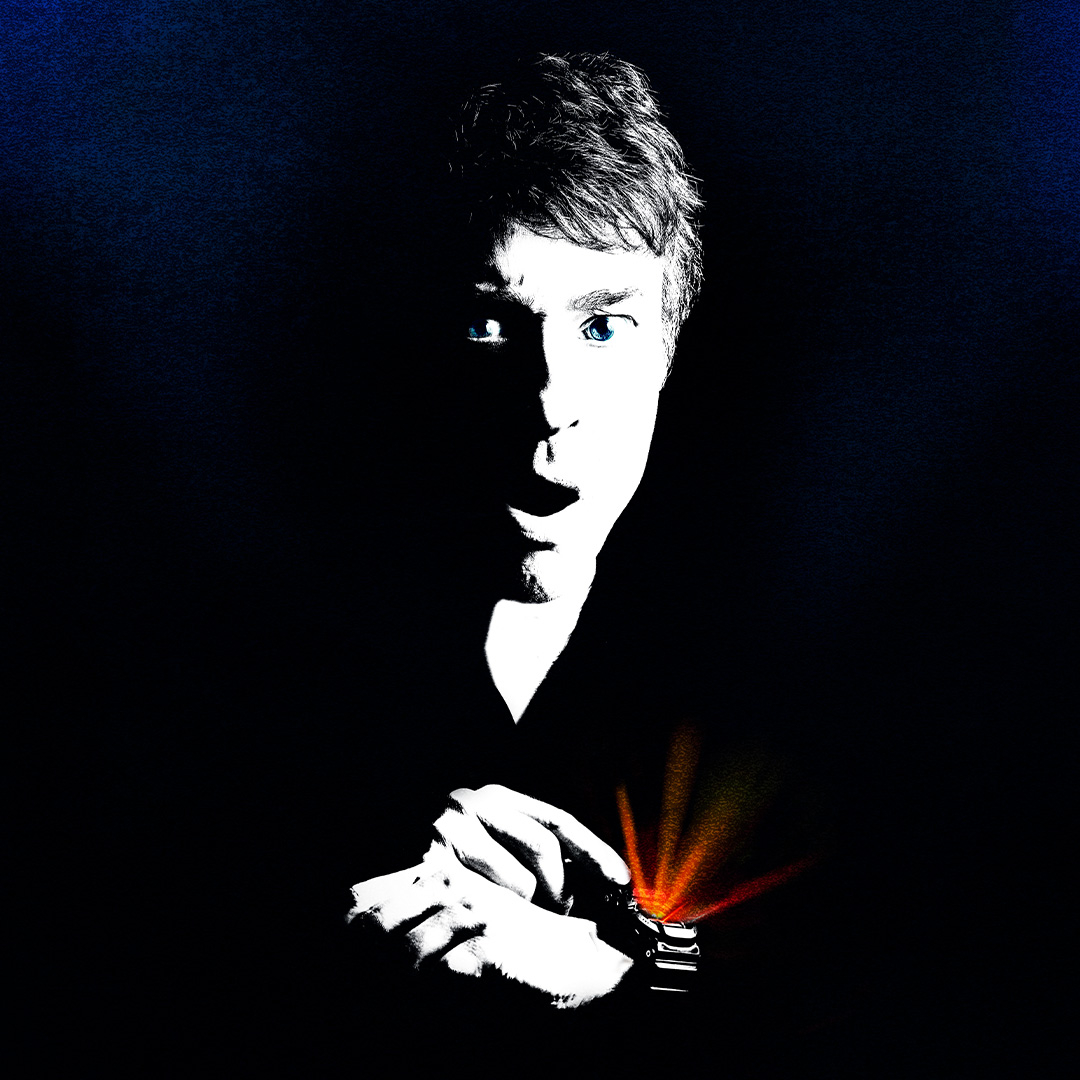 A dramatic, high-contrast portrait of a short-haired person dressed in black, with vivid blue eyes and one side of their face illuminated stark white against a nearly black background. Their hands are clasped near a wristwatch emitting striking orange and red beams of light, creating a mysterious, theatrical atmosphere.