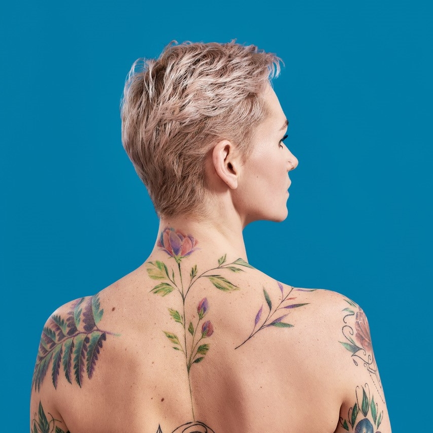 Woman with short blonde hair looks left her back  has got several tattoos - Amy's Tattoo