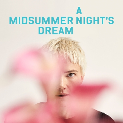 A Midsummer Night's Dream - Blonde girl with pixie hair cut looks at camera from behind a flower
