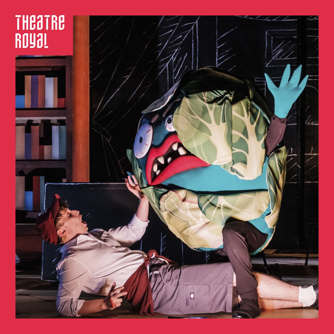 Photo: Robert Catto A large puppet cabbage stands over a man who is lying on the floor.