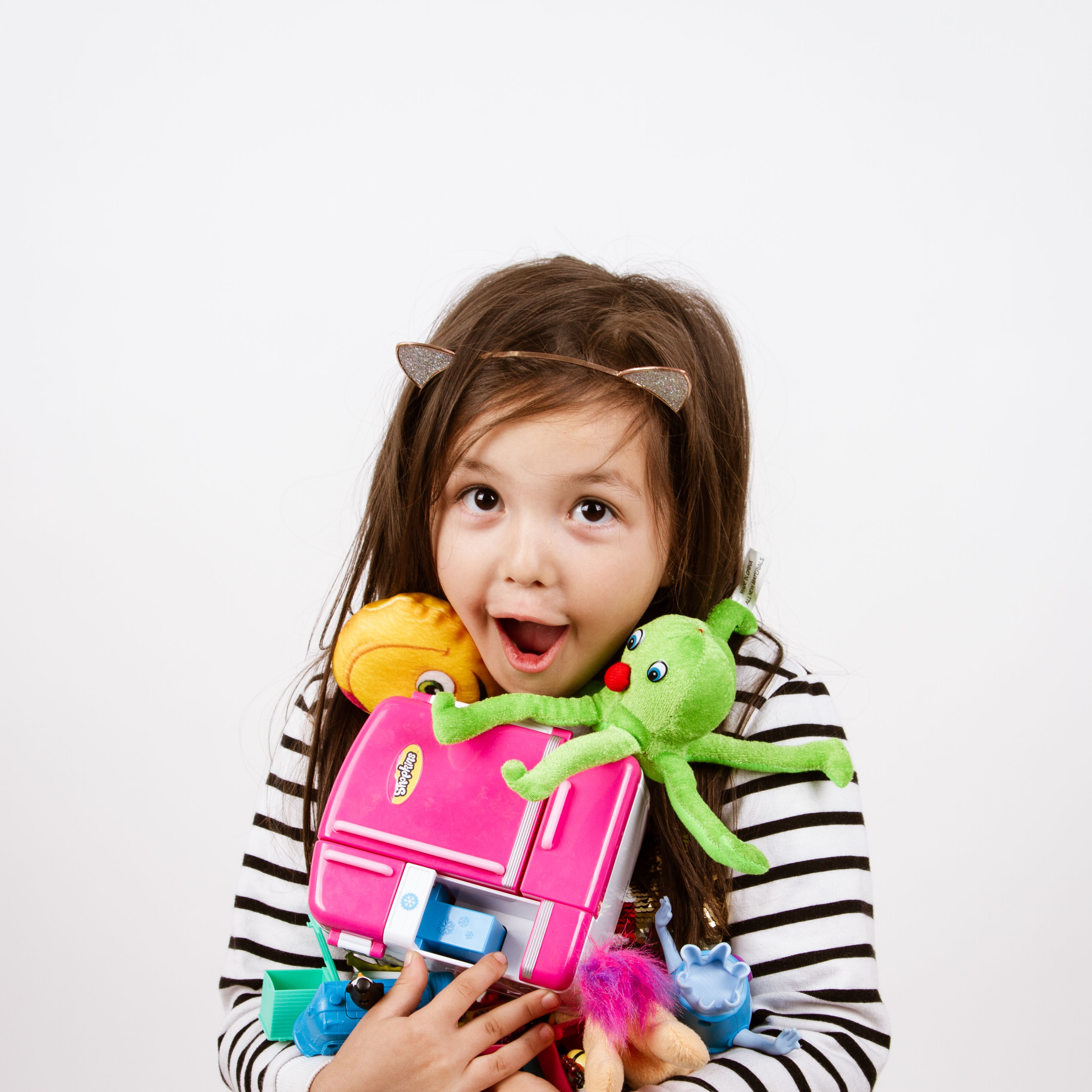 Photo: Lana Nguyen A young child holds a bunch of brightly coloured toys in their arms. They wear a black and white striped top and a headband which has cats ears on it.