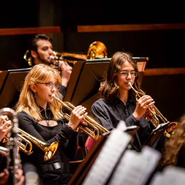 Three members of an orchestra. Two members are playing the trumpet. One is playing the trombone.