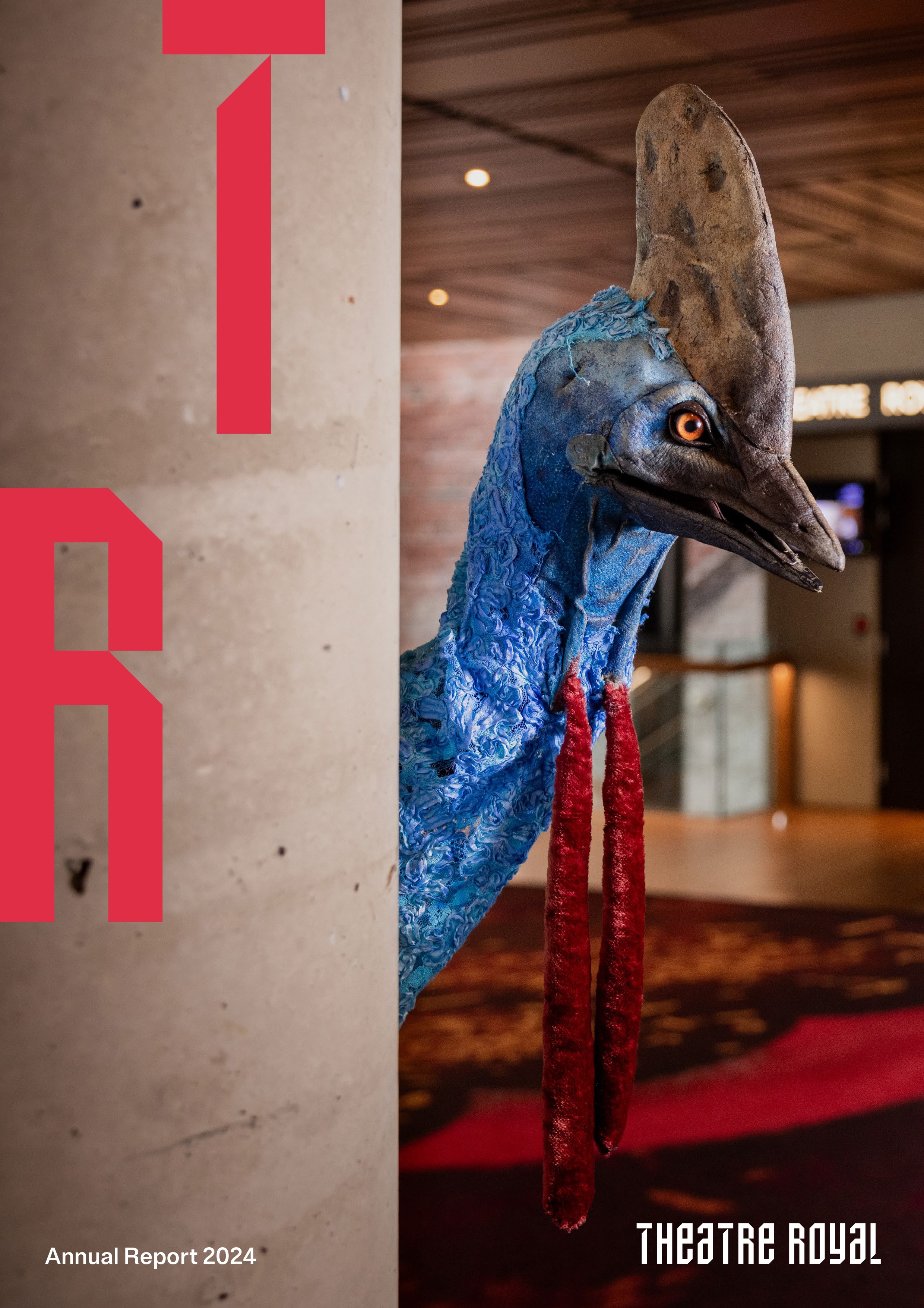 An image of a puppet of a cassowary peeks around a column in the foyer of the Theatre Royal. There is a red T and R overlayed. Annual report 2024 and the Theatre Royal logo sit at the bottom of the image in white.  