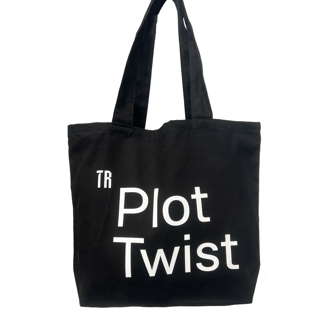 A black back in front of a white background. The bag has white writing which says Plot Twist on it and the Theatre Royal logo 'TR' in the top left side. Plot Twist is quite large on the bag.