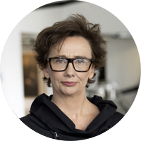 An image of Virginia Lovett looking directly to camera. She wears large, dark spectacles and she has short, dark hair. 