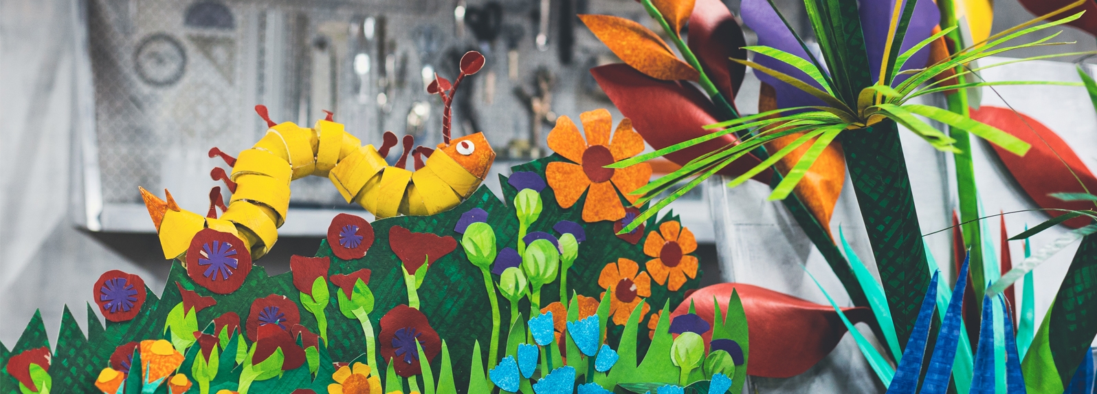 A brightly coloured caterpillar made from paper sits in a brightly coloured paper garden.