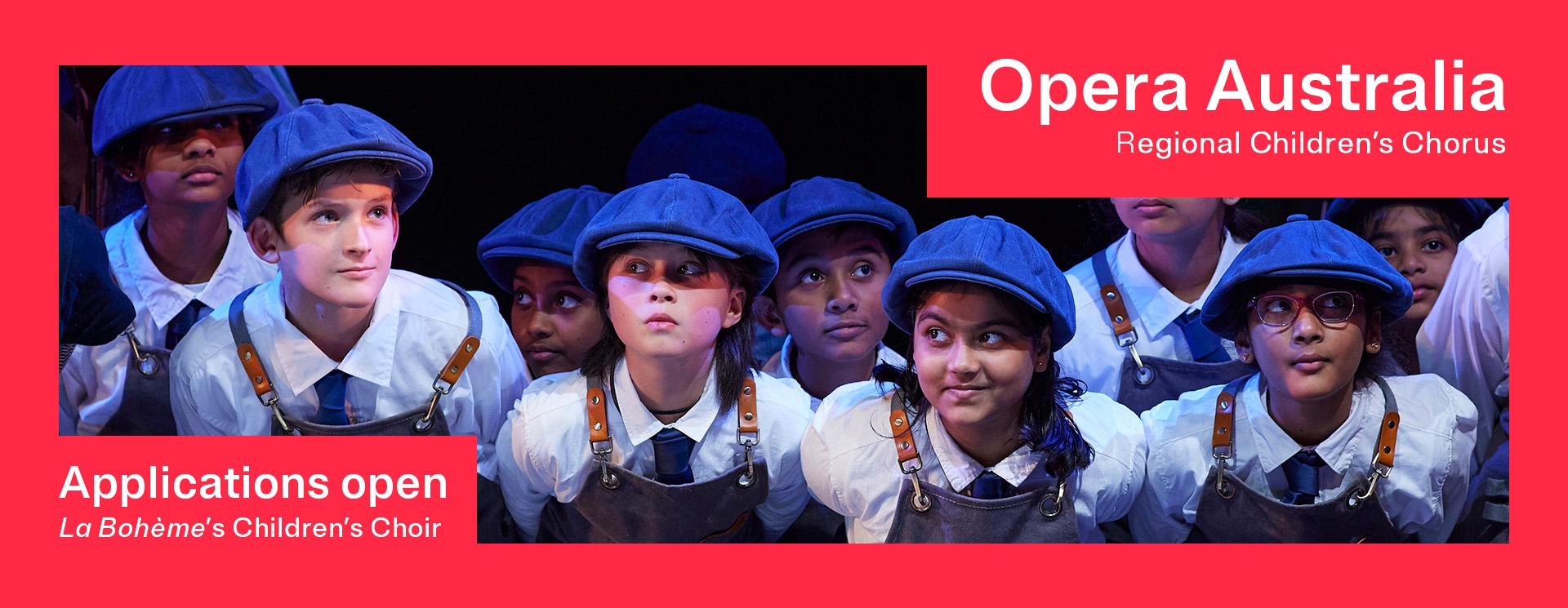 A group of childfen stand in a cluster performing on stage. They are wearing blue berrets and aprons