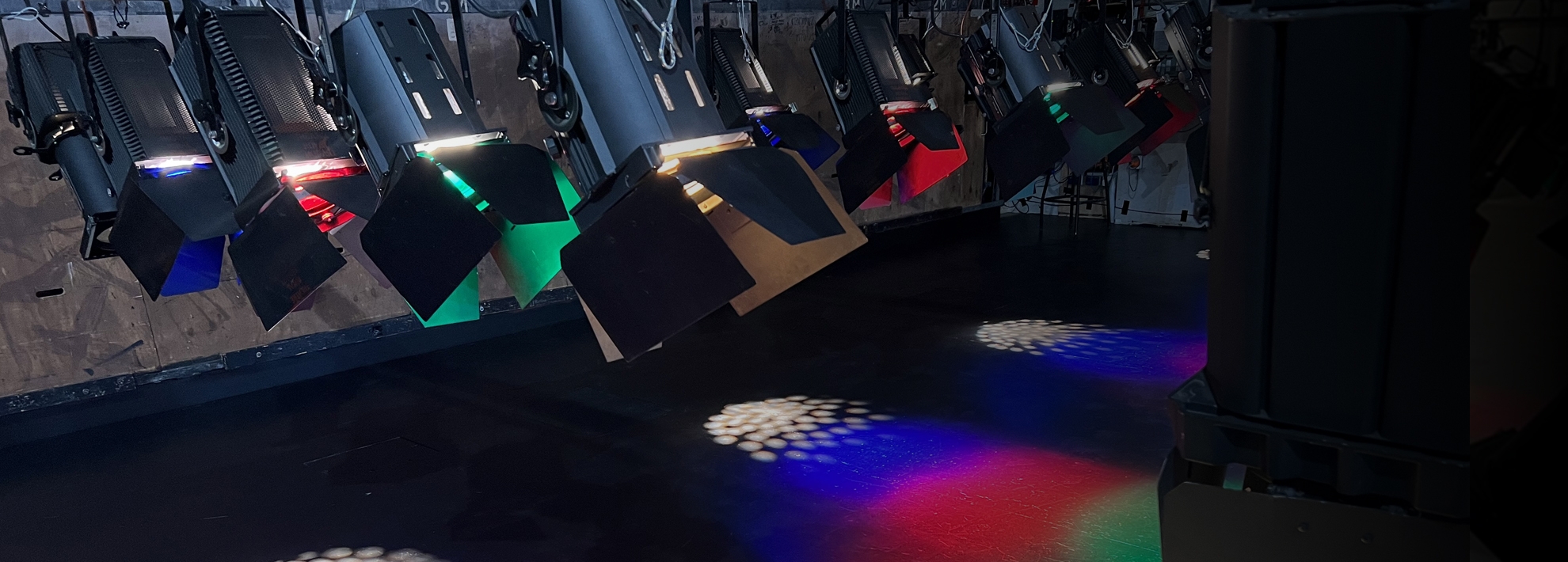 A close up shot of a theatre lighting rig, colourful beams shine on to the stage floor.